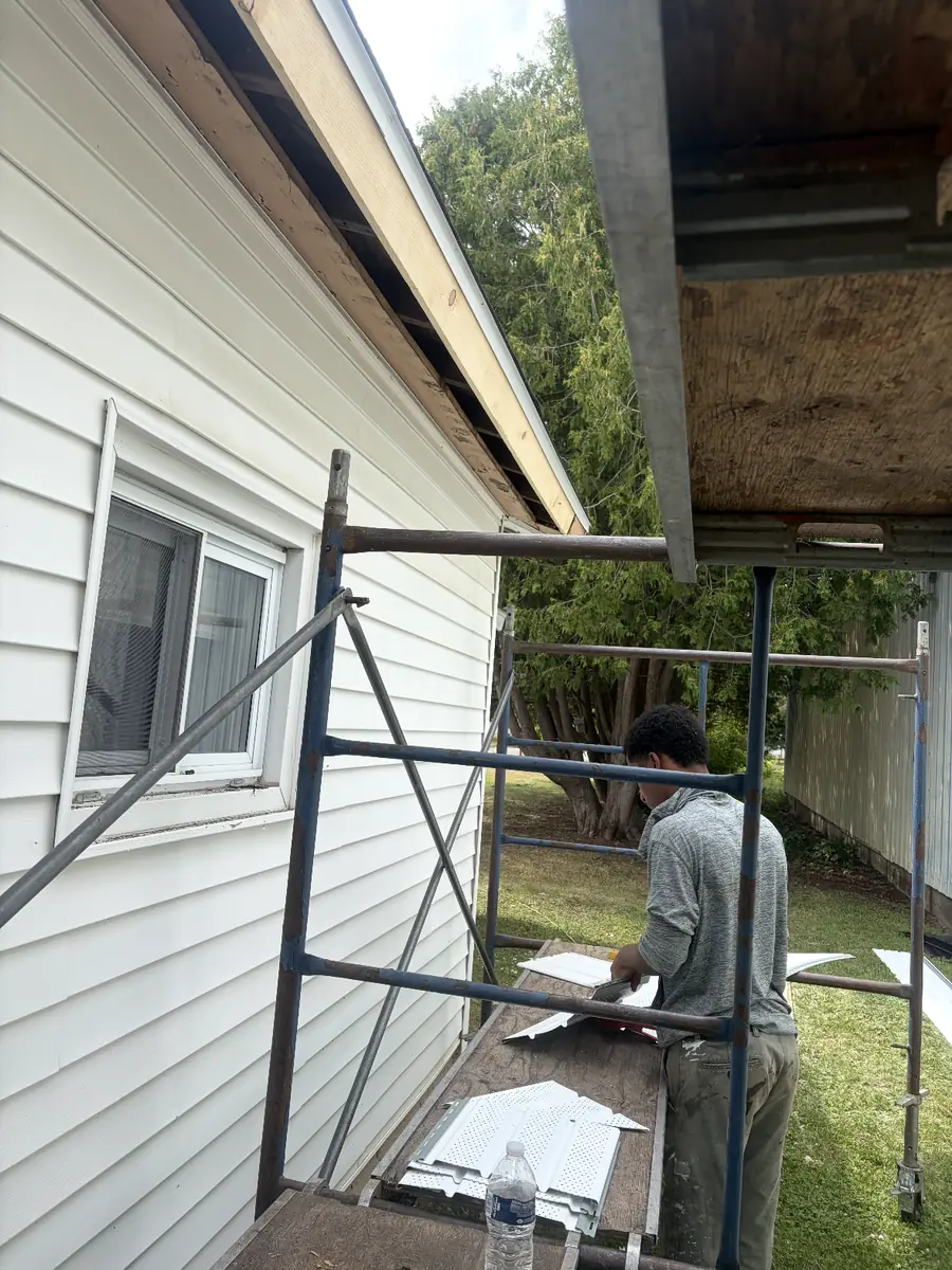 AA Roofing crew member cutting new soffit panels on a scaffold
