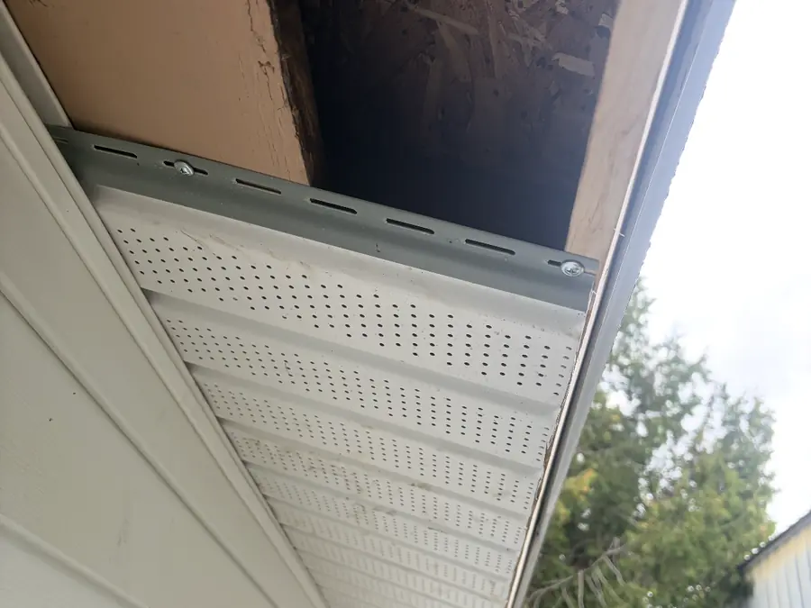 New perforated vinyl soffit being installed under an open roof eave